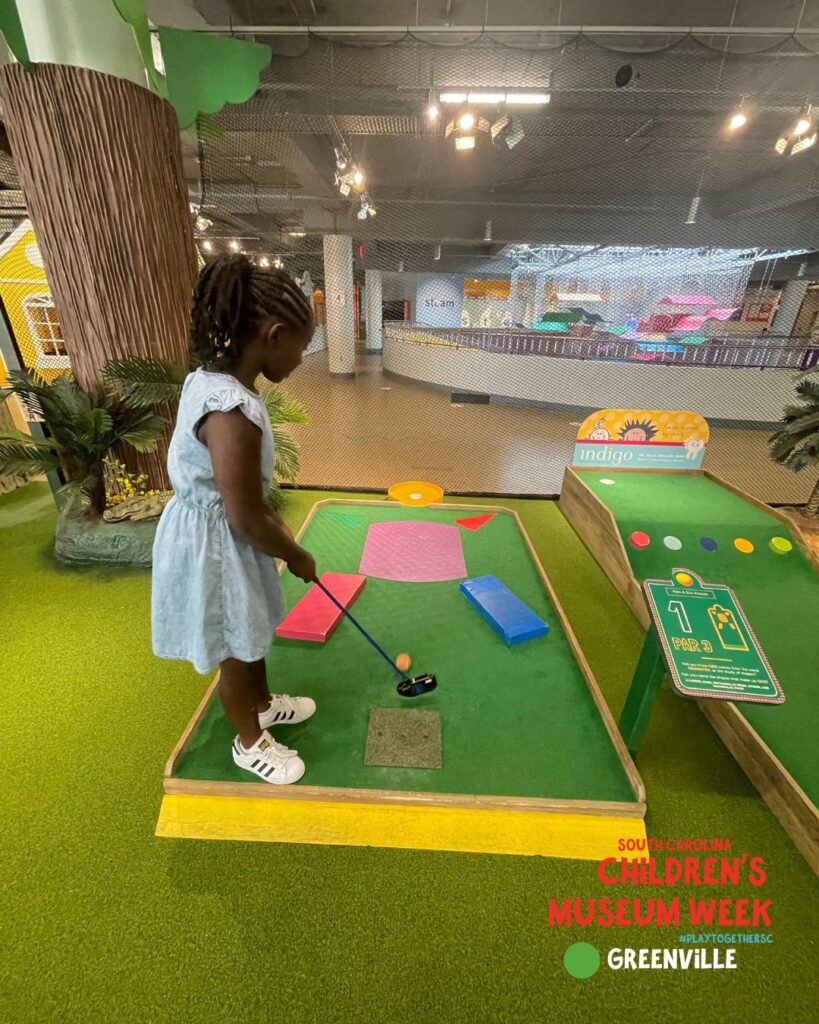 a little girl playing mini golf in the children's museum