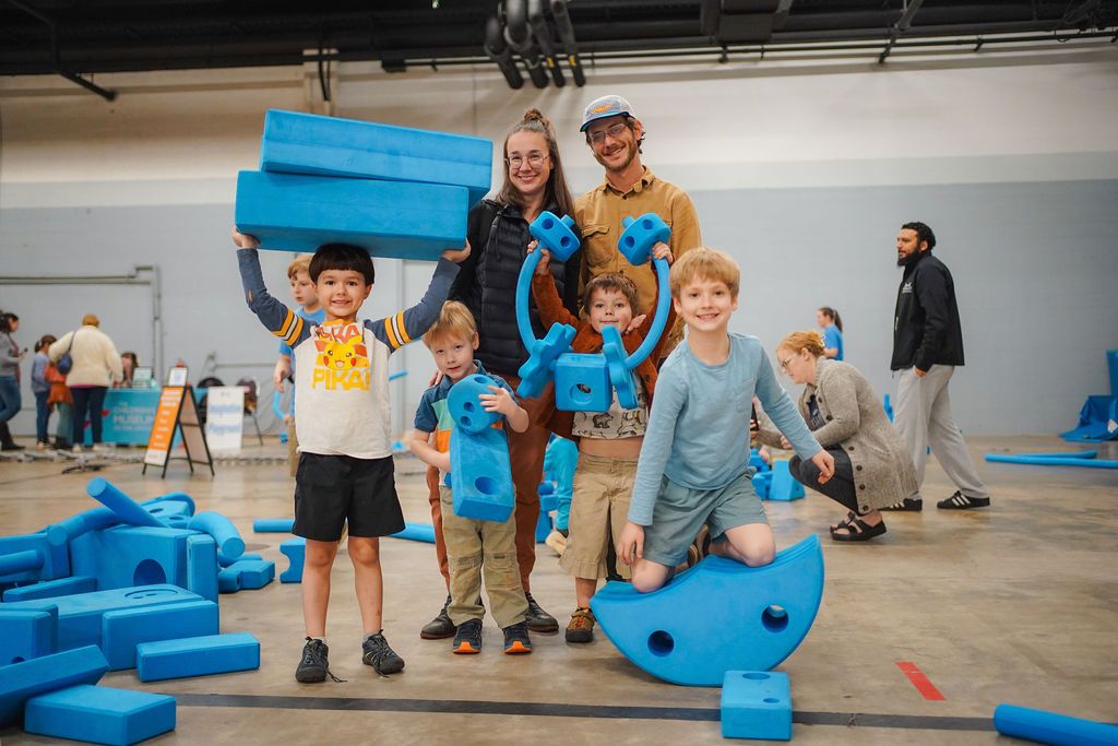 Family holding imagination playground blocks and smiling at the Children's Museum of the Upstate outreach.
