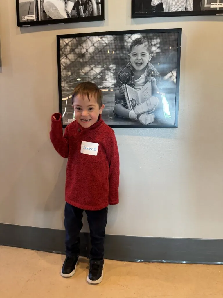 a young boy standing next to a wall with pictures on it