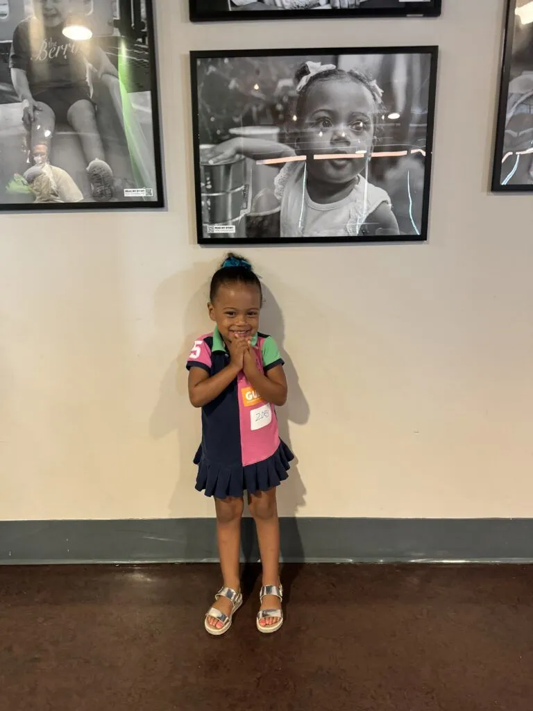a young girl standing in front of a wall with pictures on it