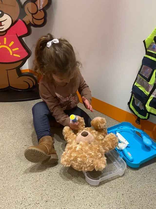a little girl sitting on the floor playing with a teddy bear