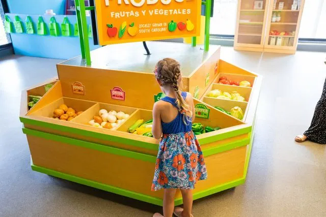a little girl standing in front of a fruit stand