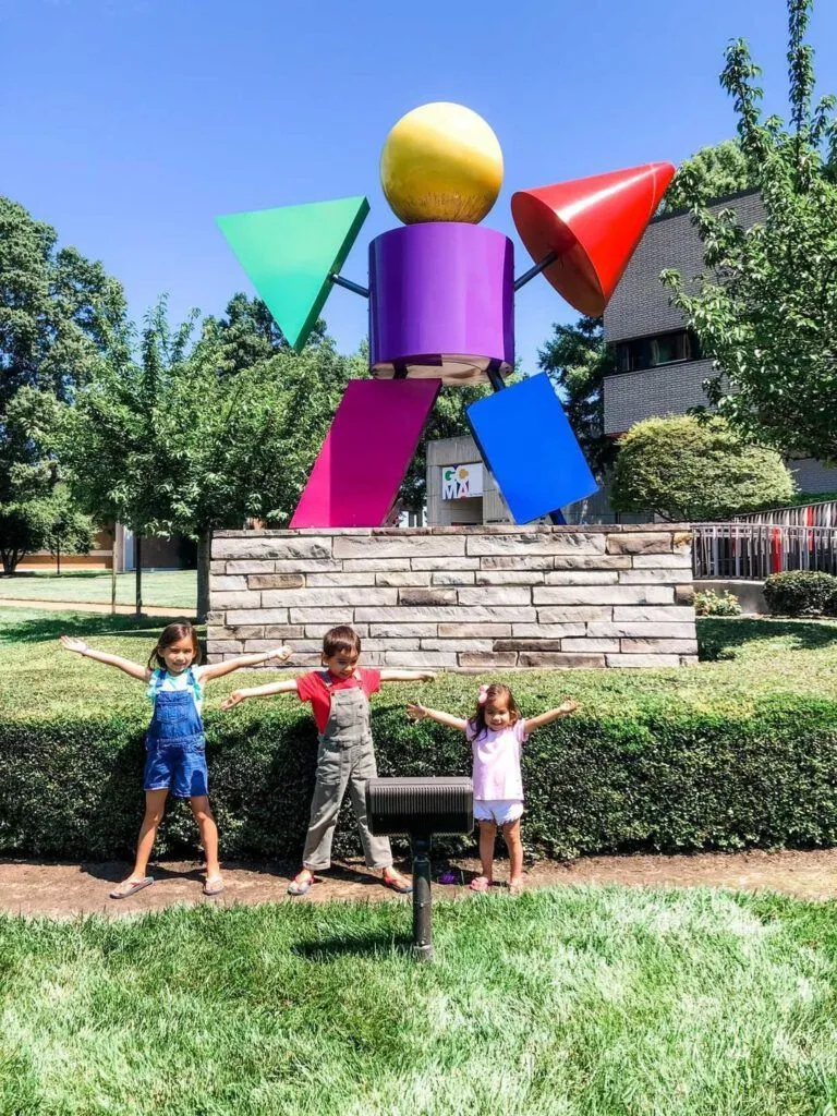 a group of children standing in front of a sculpture