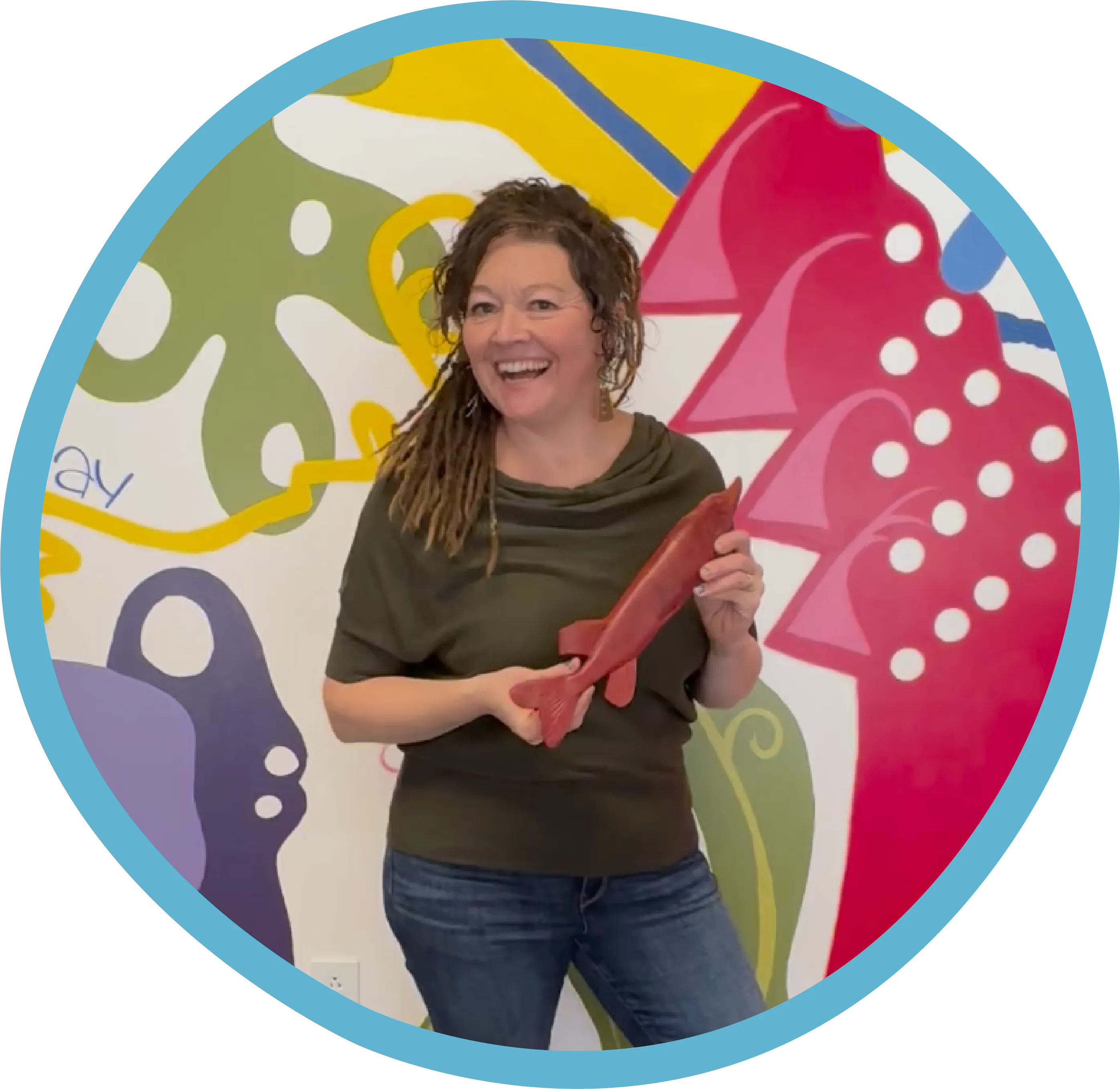 a woman holding a toy fish in front of a wall that is colorful