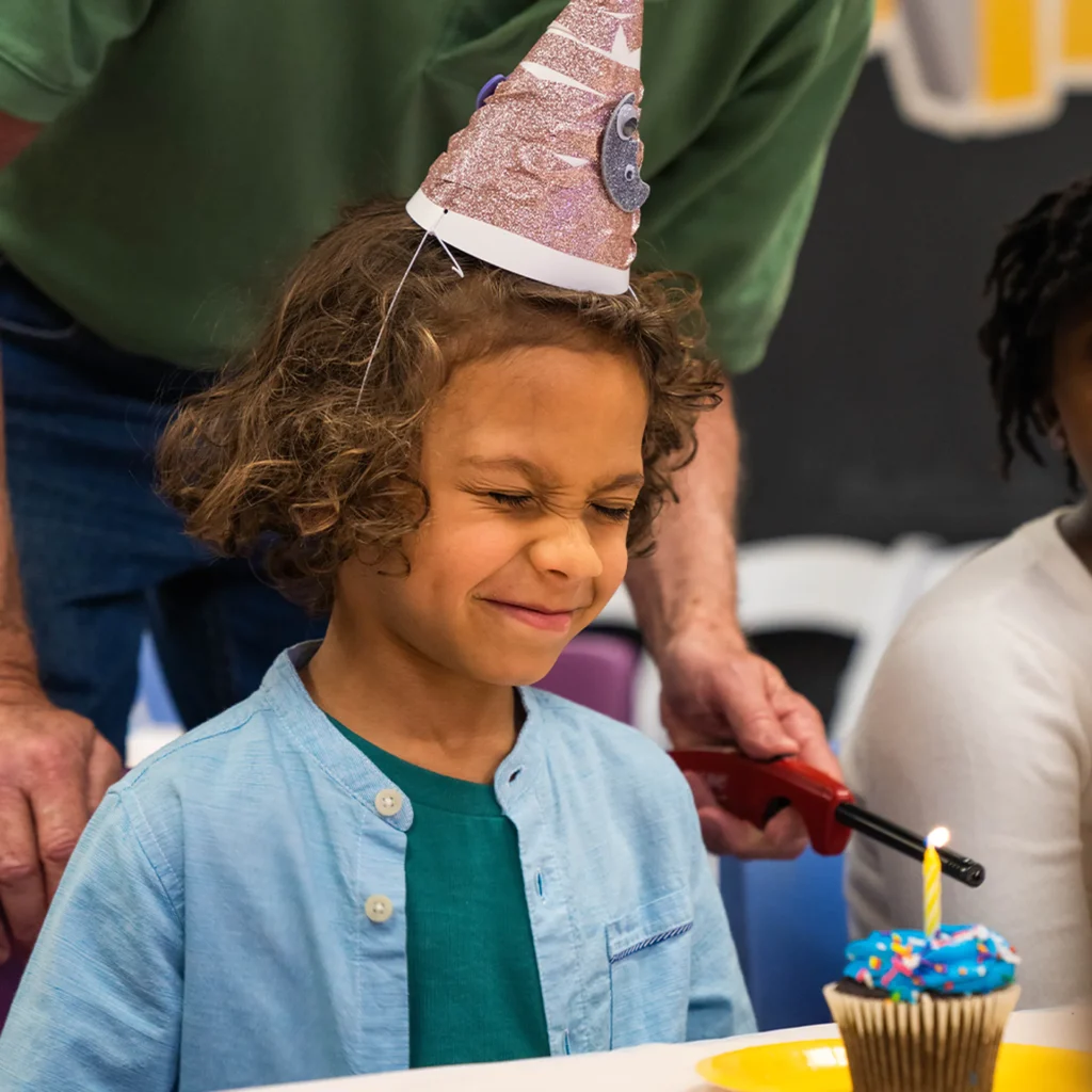 Birthday boy closing his eyes and making a wish before blowing out his candle Children's Museum of the Upstate Greenville location.