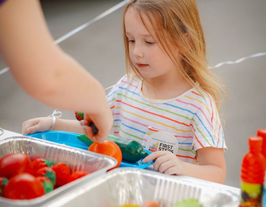 The child is served toy vegetables like tomatoes and carrots peppers and cucumbers