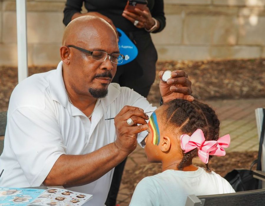 man paints a young girls face with a rainbow design