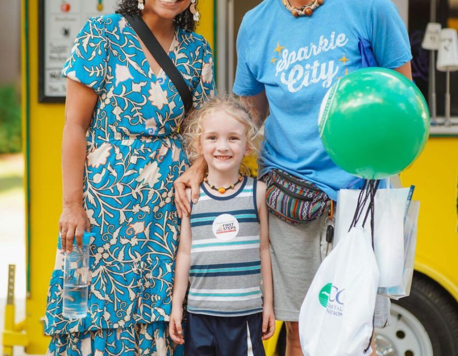 family smiles while holding a green balloon